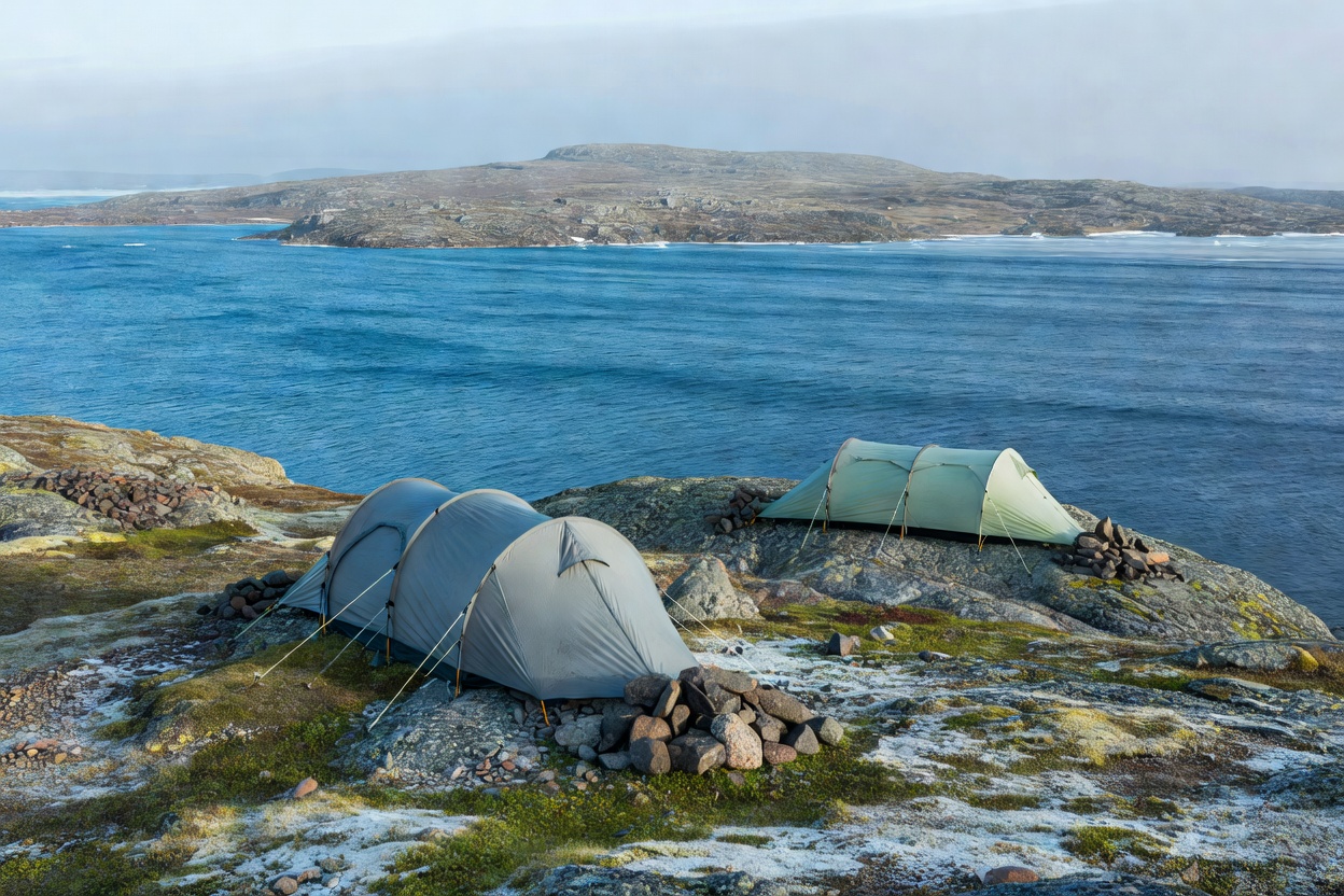 Two mountaineering tunnel tents anchored with stones on an Arctic fell beside cold blue waters